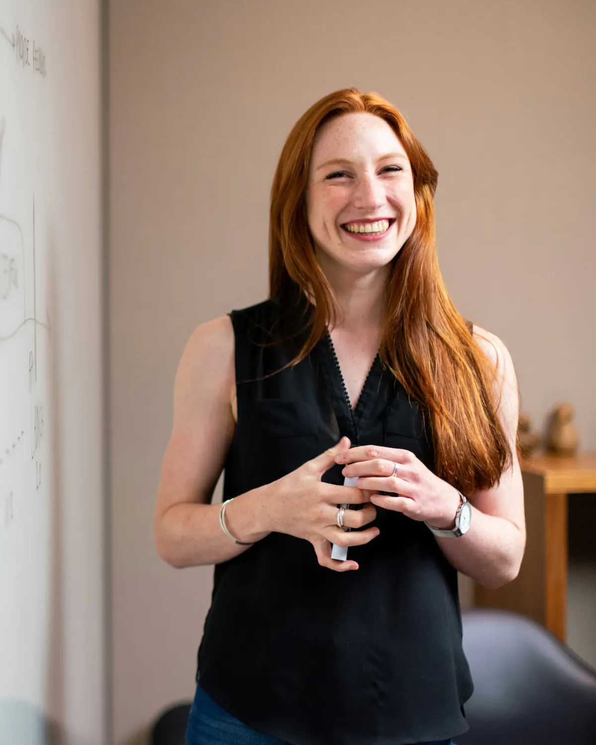 Profesora pelirroja sonriendo junto a una pizarra blanca con diagramas