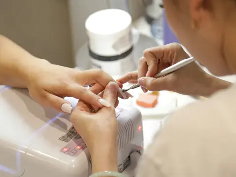 Manicura limando las uñas de una clienta en una mesa con lámpara UV