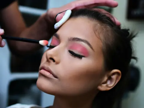 Maquilladora aplicando sombra rosa en los párpados de una modelo con los ojos cerrados