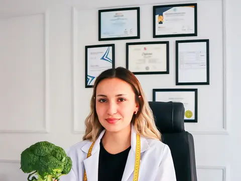 Nutricionista con guardapolvo sonriendo en su consultorio, con sus diplomas en la pared