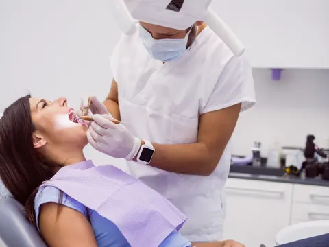 Odontólogo con barbijo trabajando en la boca de una paciente recostada en el sillón