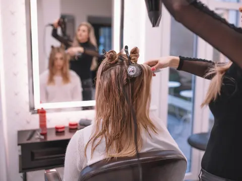 Peluquera con secador trabajando sobre el pelo de una clienta frente al espejo