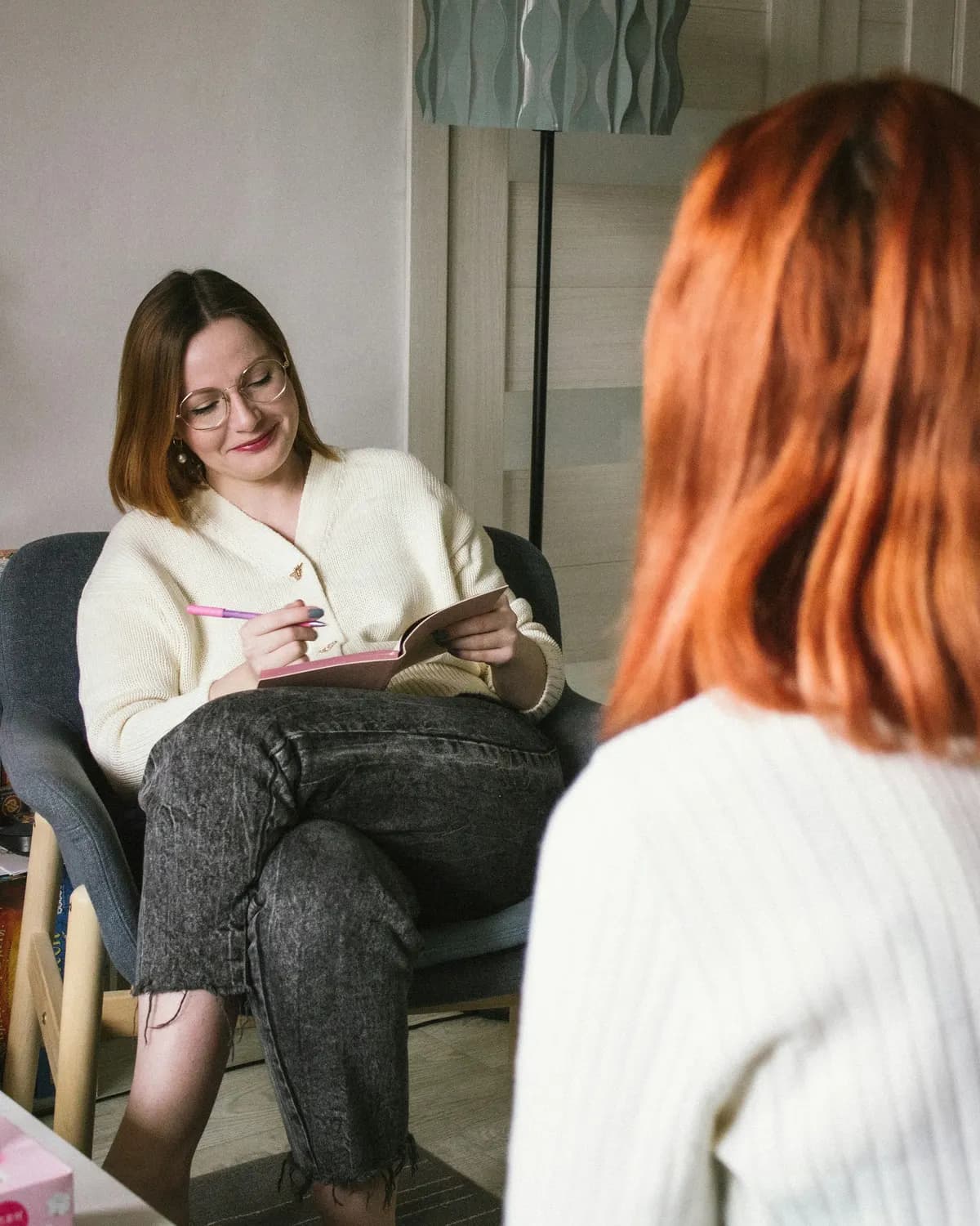 Psicóloga tomando notas en un sillón durante una sesión, con la consultante de espaldas en primer plano