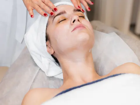 Esteticista masajeando la frente de una clienta con toalla en la cabeza en un spa