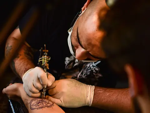Tatuador con guantes tatuando el brazo de un cliente en su estudio